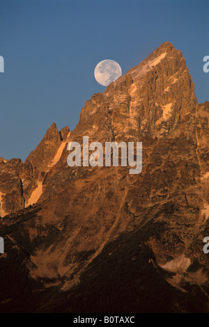 Full moon setting over the summit of the Grand Teton mountain at sunrise Grand Teton National Park Wyoming Stock Photo