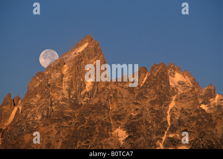 Full moon setting over the summit of the Grand Teton mountain at sunrise Grand Teton National Park Wyoming Stock Photo