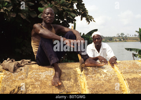 Abidjan, Ivory Coast, Cote d'Ivoire, West Africa. Burkinabe Laborer, Friend on Rest Break from Stripping Bark from Logs. Stock Photo