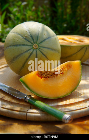 Fresh cut Cantaloupe melon whole and cut on a wood table in a garden setting Stock Photo