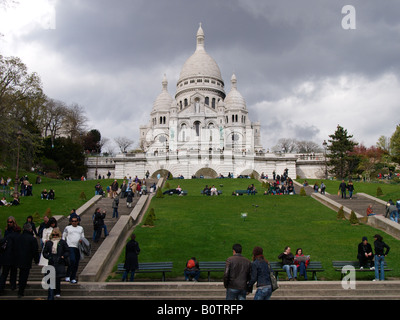 Sacre Coeur holy heart church in Montmartre Paris France with many people tourists on the steps and grass Stock Photo