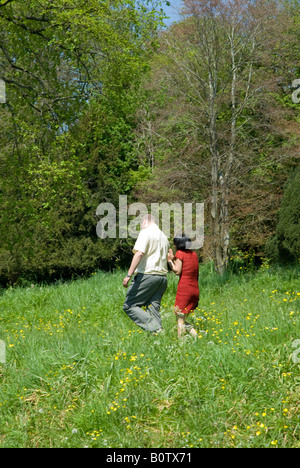 Couple walking away in long grass and wild flowers. Casual clothes and red dress Stock Photo