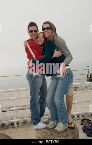 three young people smiling hugging having a good time on Aberystwyth promenade wales UK Stock Photo