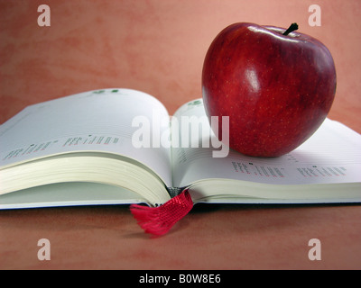 Red apple on an open book or day-planner with red bookmark Stock Photo