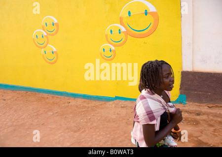 Young girl passing a house painted in the colours of the Mozambiqan telelephone company Mcel. Mozambique. Stock Photo