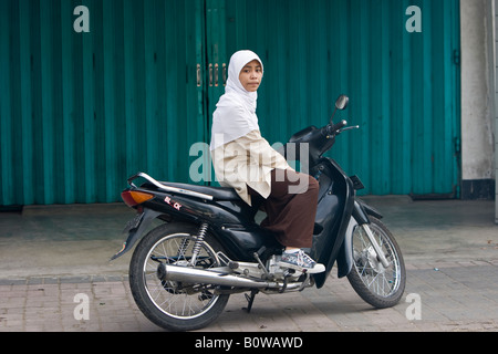 Young Muslim woman sitting on a moped, Mataram, Lombok Island, Lesser Sunda Islands, Indonesia Stock Photo