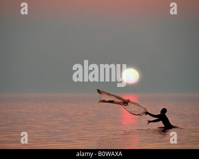 Fisherman standing in the bay casting his net beneath the setting sun, Lombok Island, Lesser Sunda Islands, Indonesia Stock Photo
