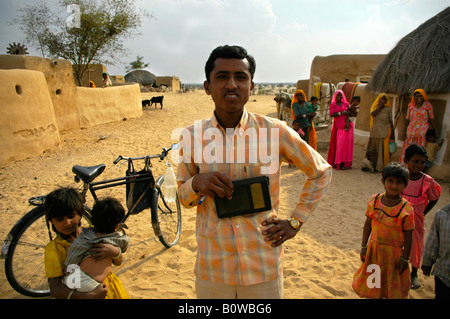 Young Indian man holding a radio standing in front of a bicycle among other people in a village in the Thar Desert near Jaisalm Stock Photo