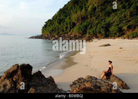 Young woman sitting alone on a rock on an empty beach, Koh Kradan, Thailand, Southeast Asia Stock Photo