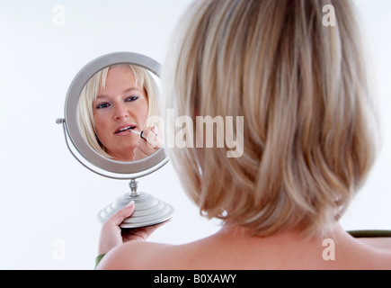 blond woman paints her face in the mirror Stock Photo
