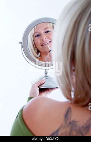 blond woman paints her face in the mirror Stock Photo