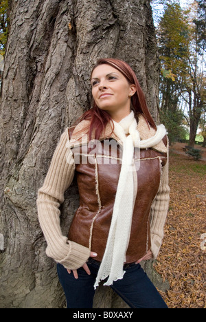 young woman in autumn leaning against tree trunk Stock Photo