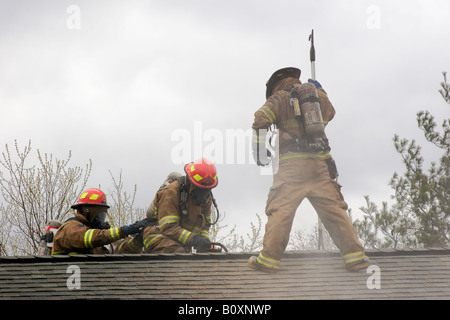 Firefighter trainees cut a hole in the roof of a burning house Stock Photo