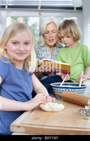 Granddaughter (8-9) smiling, Grandmother and grandson (8-9) in background Stock Photo