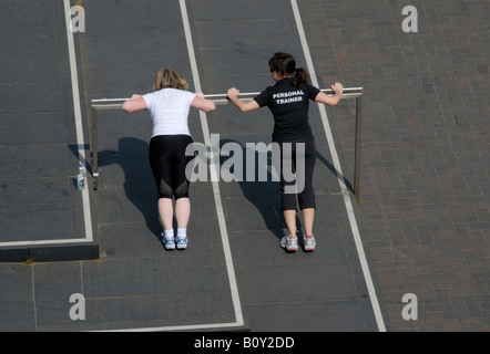 Personal trainer (indicated on the back of her t-shirt) and client doing push ups on raised bar, South Bank, London, England Stock Photo