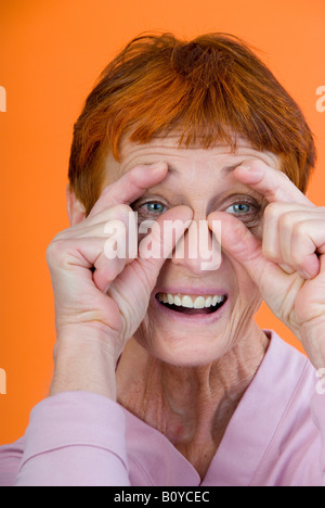 older woman having fun, looking through glasses made with her fingers Stock Photo