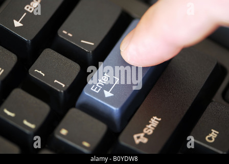 Macro of computer keyboard with finger pressing enter key Stock Photo