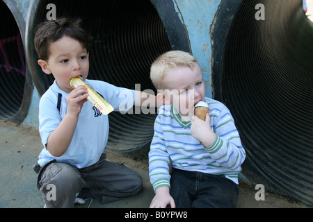 2 small children sitting in a park eating lollies and ice cream Stock Photo