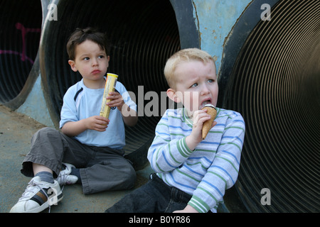 Two 3 year old boys sitting in a park eating lollies Stock Photo