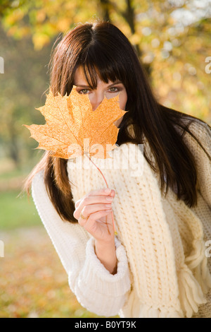 Brunette woman hiding behind autumn leaf, portrait Stock Photo