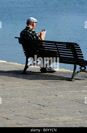 Tourist doing a newspaper puzzle Mandraki Rhodes Greece Stock Photo