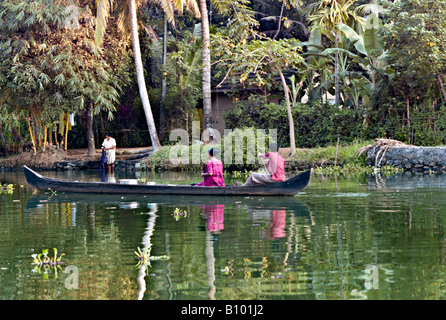 INDIA KERALA Young Indian couple rowing their wooden boat down the backwaters of Kerala as they pass by a woman washing clothes Stock Photo