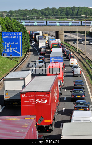 Transport choice M25 motorway congestion slow moving traffic jam watching fast passenger train railway bridge junction 28 Brentwood Essex England UK Stock Photo