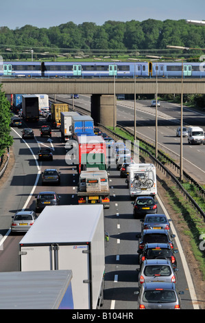 Transport choice M25 motorway congestion slow moving traffic jam watching fast passenger train railway bridge junction 28 Brentwood Essex England UK Stock Photo