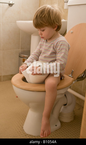 young child, boy, learning to use the toilet, loo, sitting on seat holding a paper roll, twenty seven months old Stock Photo