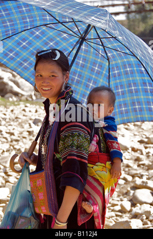 Black Hmong woman carrying baby and umbrella near Sapa Northern Vietnam Stock Photo