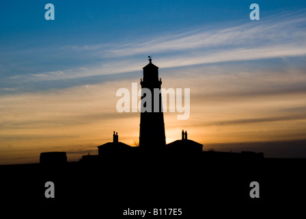 Silhouette of Happisburgh Lighthouse at sunset on the Norfolk coast, with colourful evening sky and surrounding buildings in shadow. Stock Photo