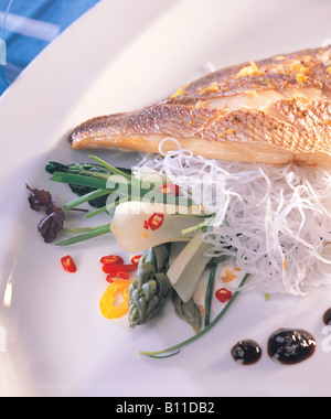 Asian style sea bream Oven dish baked golden crusty with various gratin saute vegetable selection of chili spices presented in white plate blue towel Stock Photo