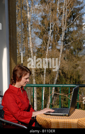 Woman sitting outside with her laptop on balcony Stock Photo