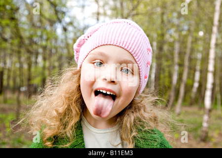 Cheerful little girl in a pink cap puts out the tongue in forest Stock Photo