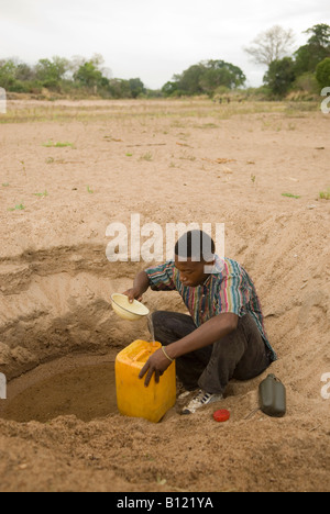 Young man pouring drinking water into a container from the water reservoir under a dry riverbed. Niassa Reserve. Mozambique. Stock Photo