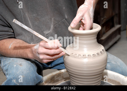 Potter decorating completed pitcher on potter's wheel Stock Photo