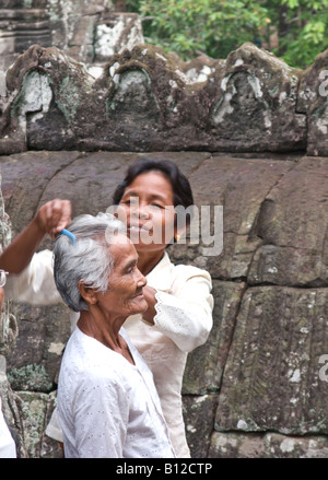 Cambodian woman combing hair of old woman prior to taking souvenir photograph, Bayon temple, Angkor Thom, Cambodia Stock Photo