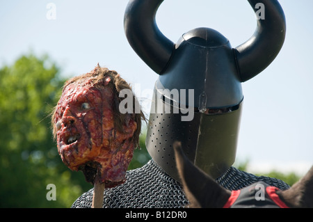 Medieval Knight wearing horned helmet, carrying a pole with a decapitated head. Stock Photo