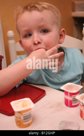 Fussy eaters a 3 year old boy eating 3 pots of fromage frais using his hands and making a mess Stock Photo
