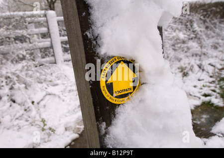 Winter walk: a snow-covered post and rail fence with yellow footpath sign in Sussex. Stock Photo