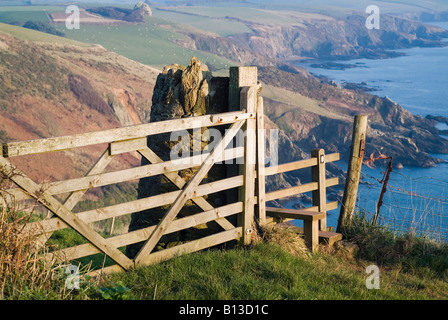 High view of the hazy cliffs on a sunny day from a wooden gate and stile on the coastal path between Mothecombe and Stoke. South Hams, Devon. UK Stock Photo
