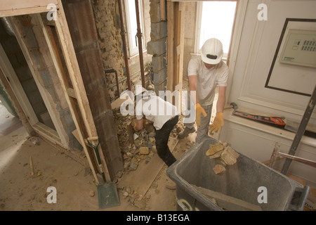 A workman throws rubble into a bin as his colleague collects more from the floor. Stock Photo