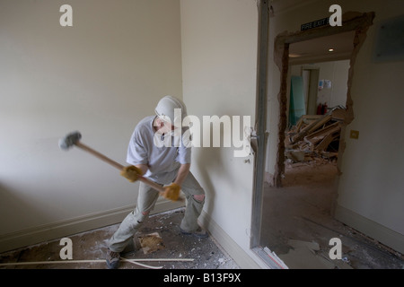 A workman swings a sledge hammer at a wall on a demolition site. Stock Photo