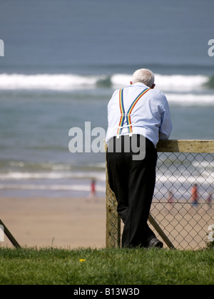 Old man leaning against the fence looking out to sea Stock Photo