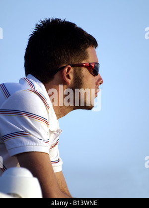 Side view of a young man wearing sunglasses, backed by a blue sky Stock Photo