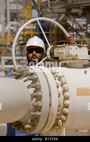 A worker turning a valve on a pipe. Bhit Gas Field, Sindh, Pakistan Stock Photo