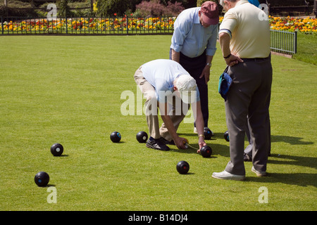 Four seniors retired elderly pensioners gentlemen retirees playing bowls on crown bowling green in public park England UK Britain Stock Photo