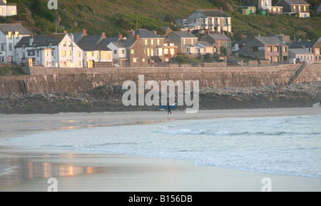 Surfers return from a late afternoon surf on Sennen beach, Cornwall. Stock Photo