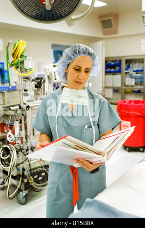 A woman surgeon wearing scrubs reviews patient medical information in a hospital operating room in Orange CA Stock Photo