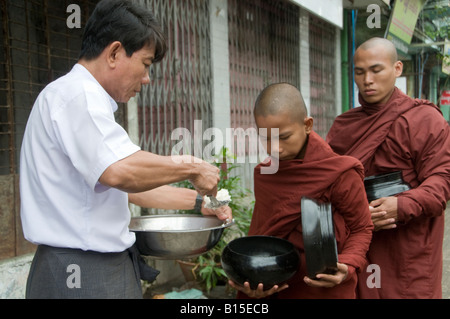 A man serving Buddhist novices rice on their morning alms walk in the city of Yangon Republic of the Union of Myanmar Stock Photo